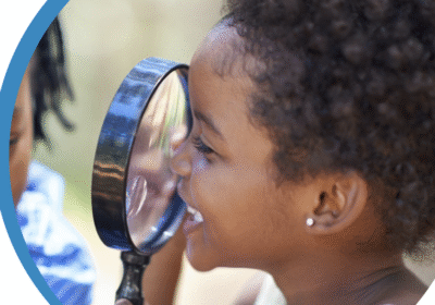 Photo of young girl looking through a magnifying glass with a smile